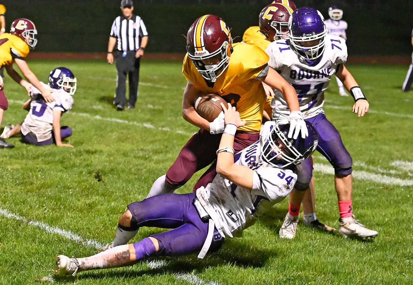 Logan Gadbois holding a football while Bourne players make contact during a game.